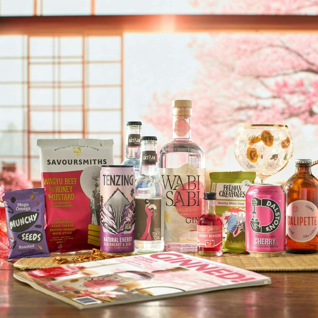 A pink and white bottle of gin sits alongside snacks, drinks and a cherry blossom background.