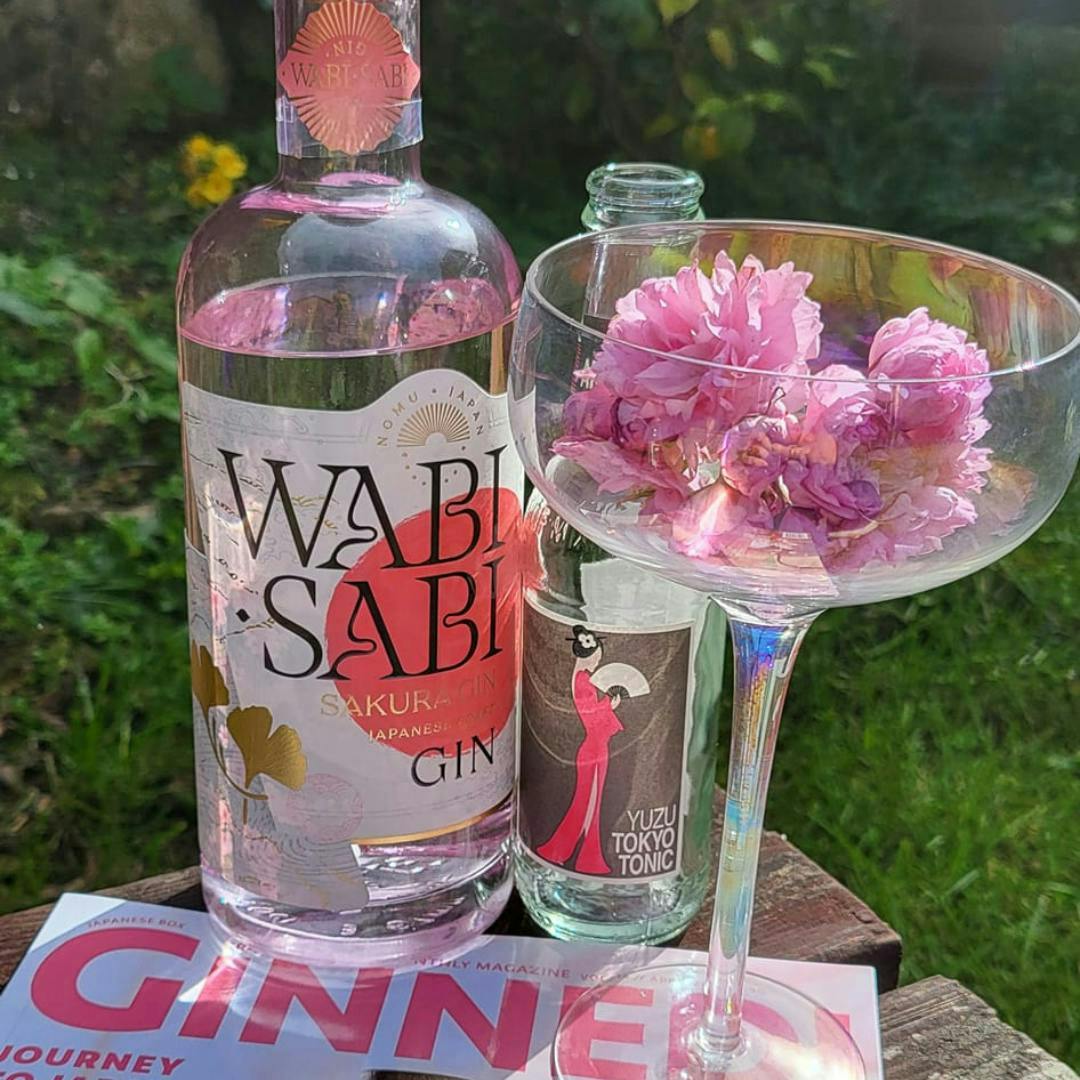 A bottle of Wabi Sabi Gin from Japan with a pink and whiet label next to a glass with cherry blossom in